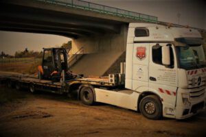 kleiner Stapler auf Tieflader unter Brücke